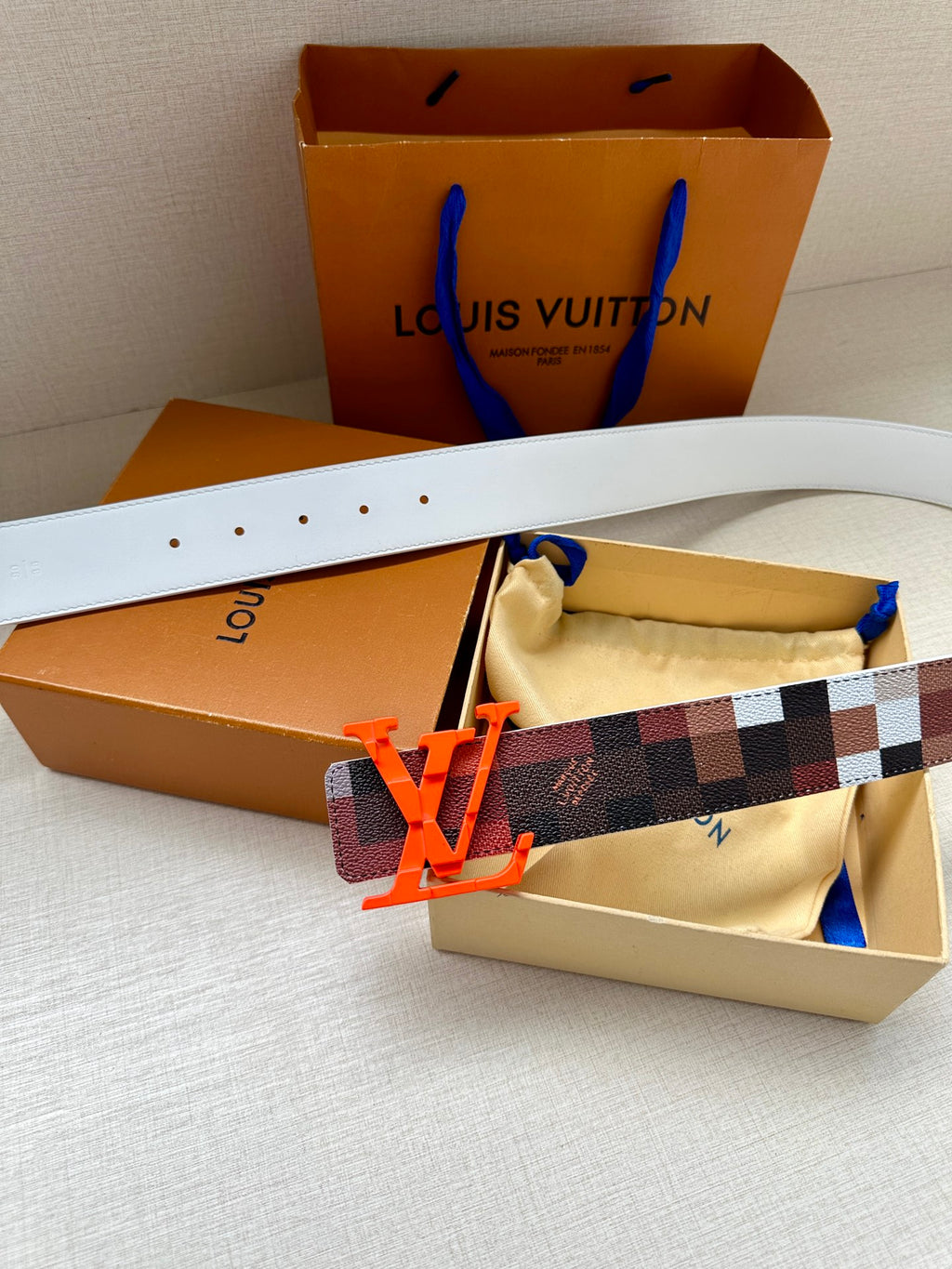 Louis Vuitton belt with dark checkered strap, white leather, orange LV buckle and stitch holes