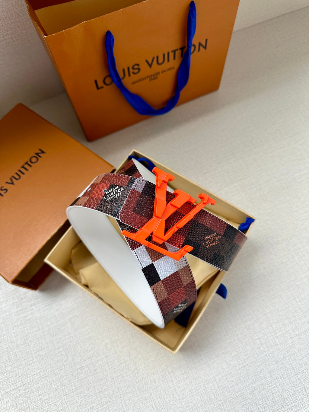 Louis Vuitton belt with dark red checkered pattern and orange LV buckle on white strap