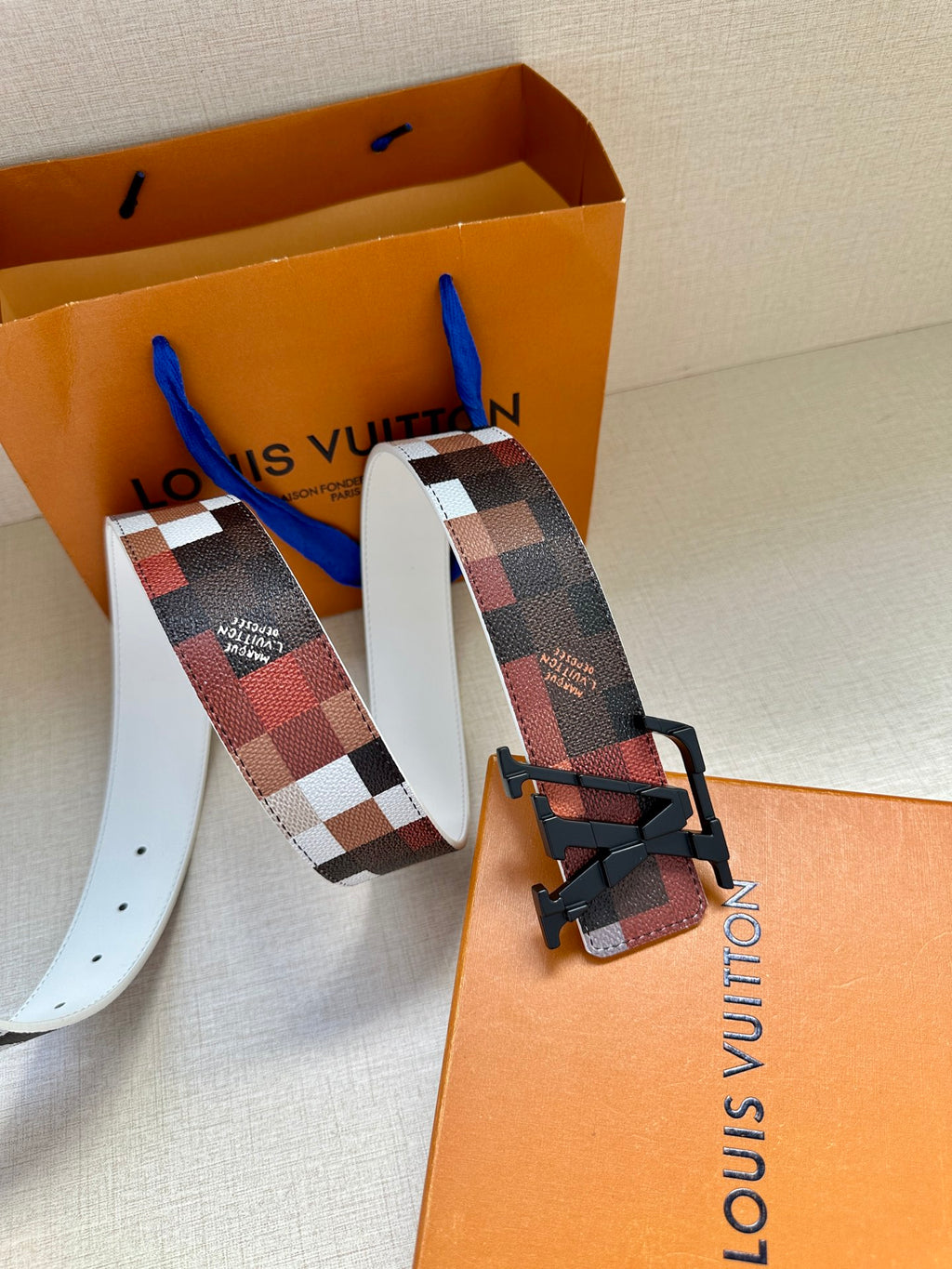 Louis Vuitton belt set with red-brown check strap, black buckle, and white strap reverse.