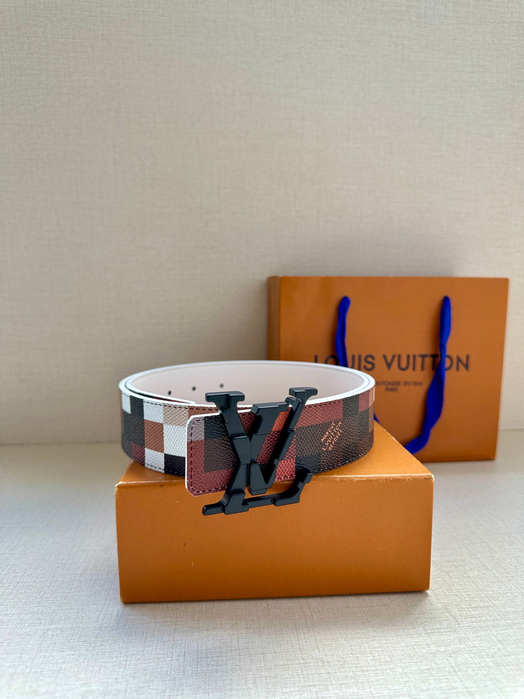 Louis Vuitton belt with red-brown check strap and bold dark V buckle, wide.