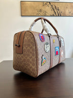 Coah duffel bag angled view, monogram canvas with brown leather trim and charm patches
