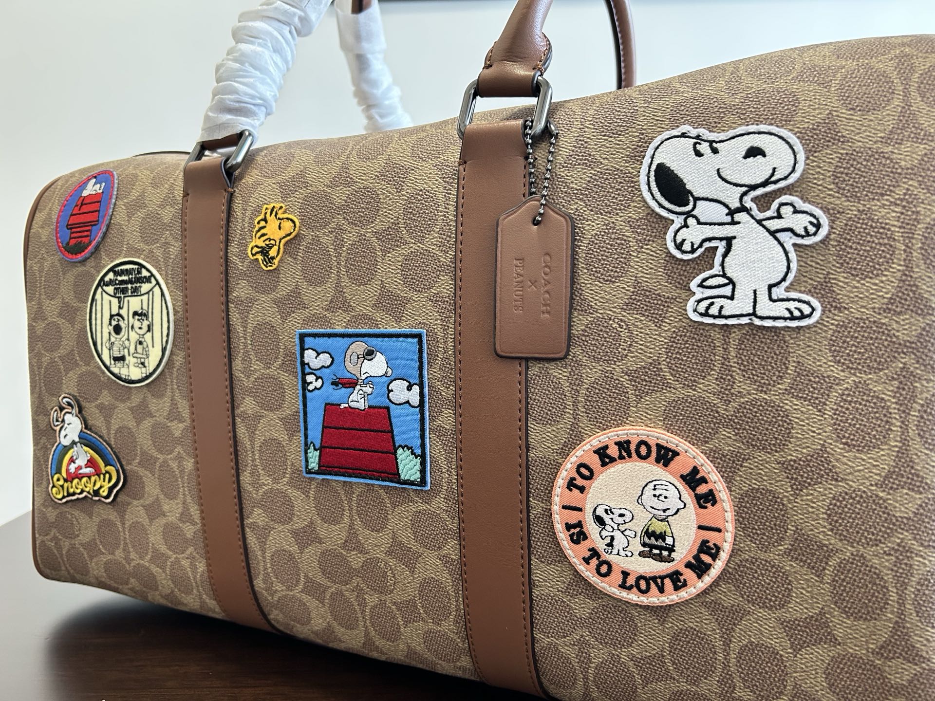 Coah duffel bag close-up, monogram canvas with patch badges and brown leather strap