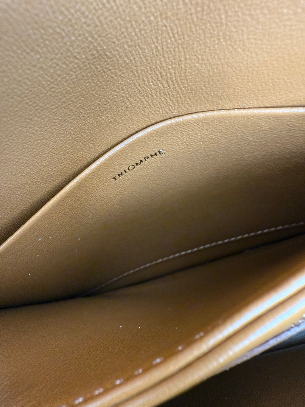 Tan leather bag interior with embossed text "TRIOMPHE" near the seam line.