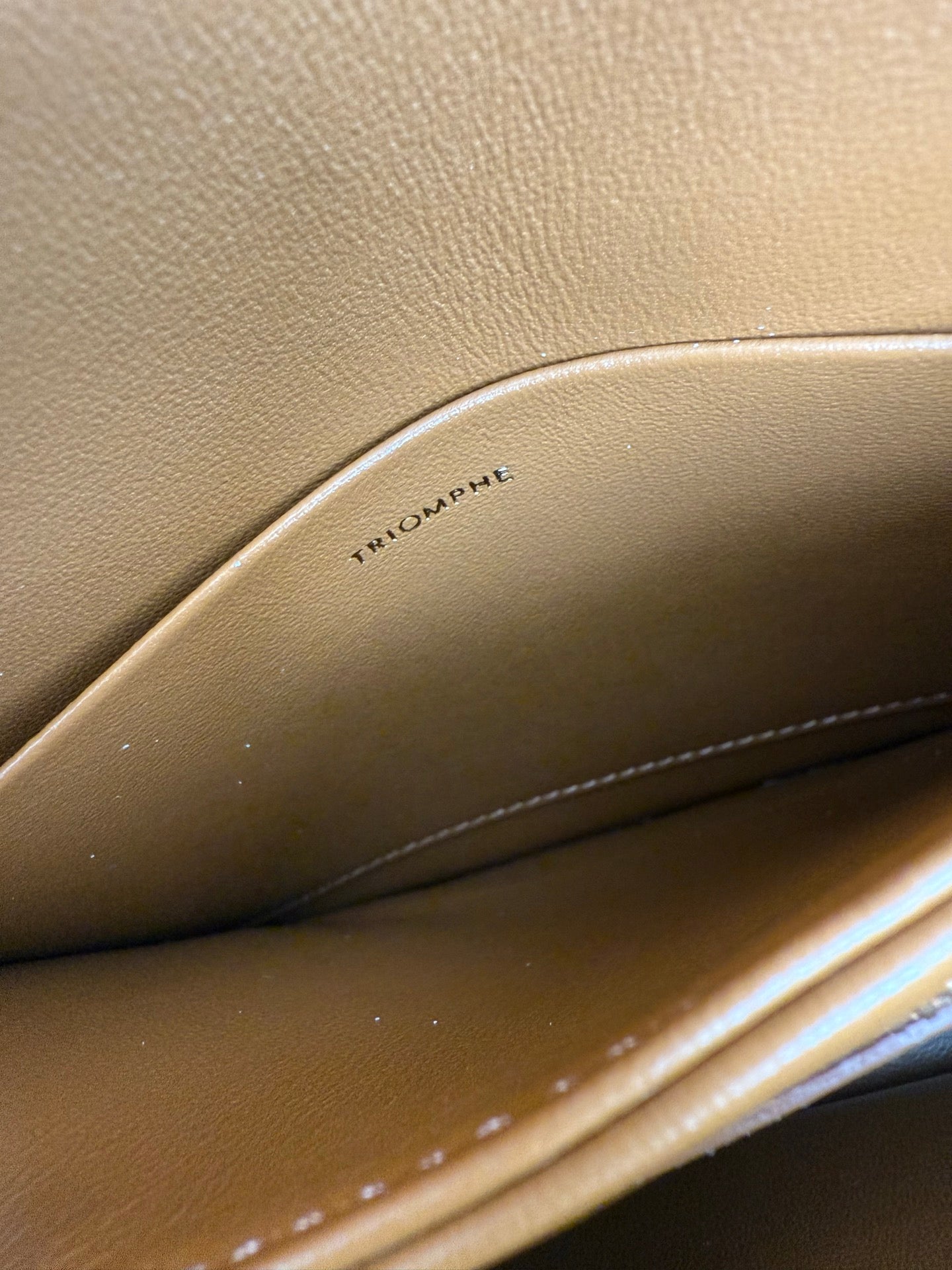 Tan leather bag interior with embossed text "TRIOMPHE" near the seam line.