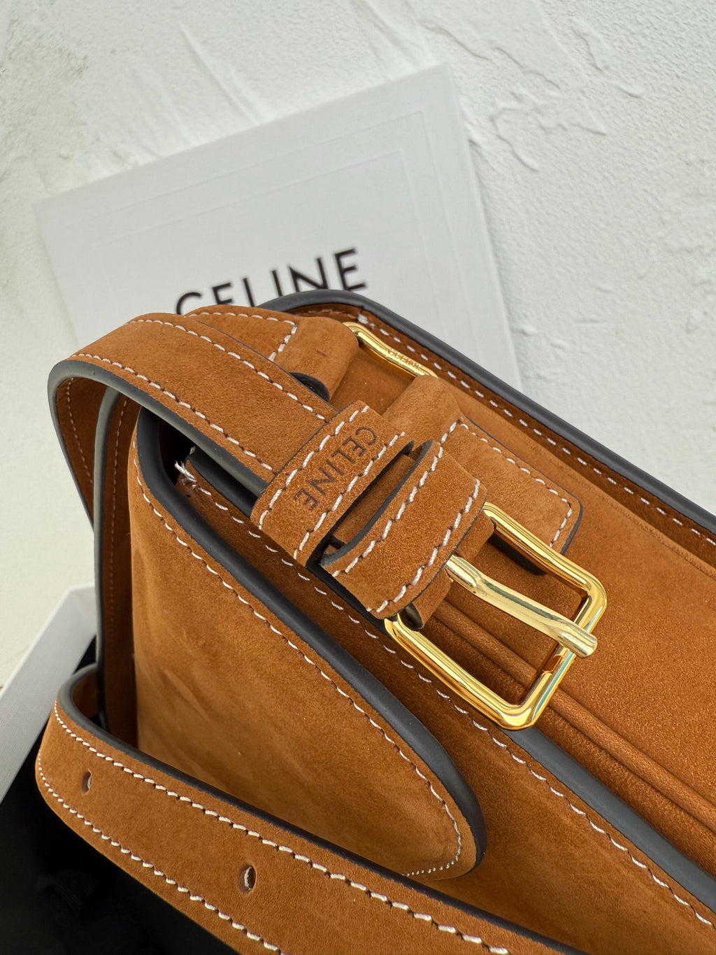 Tan suede bag with logo embossed detail, gold-tone buckle hardware, and stitched leather trim.