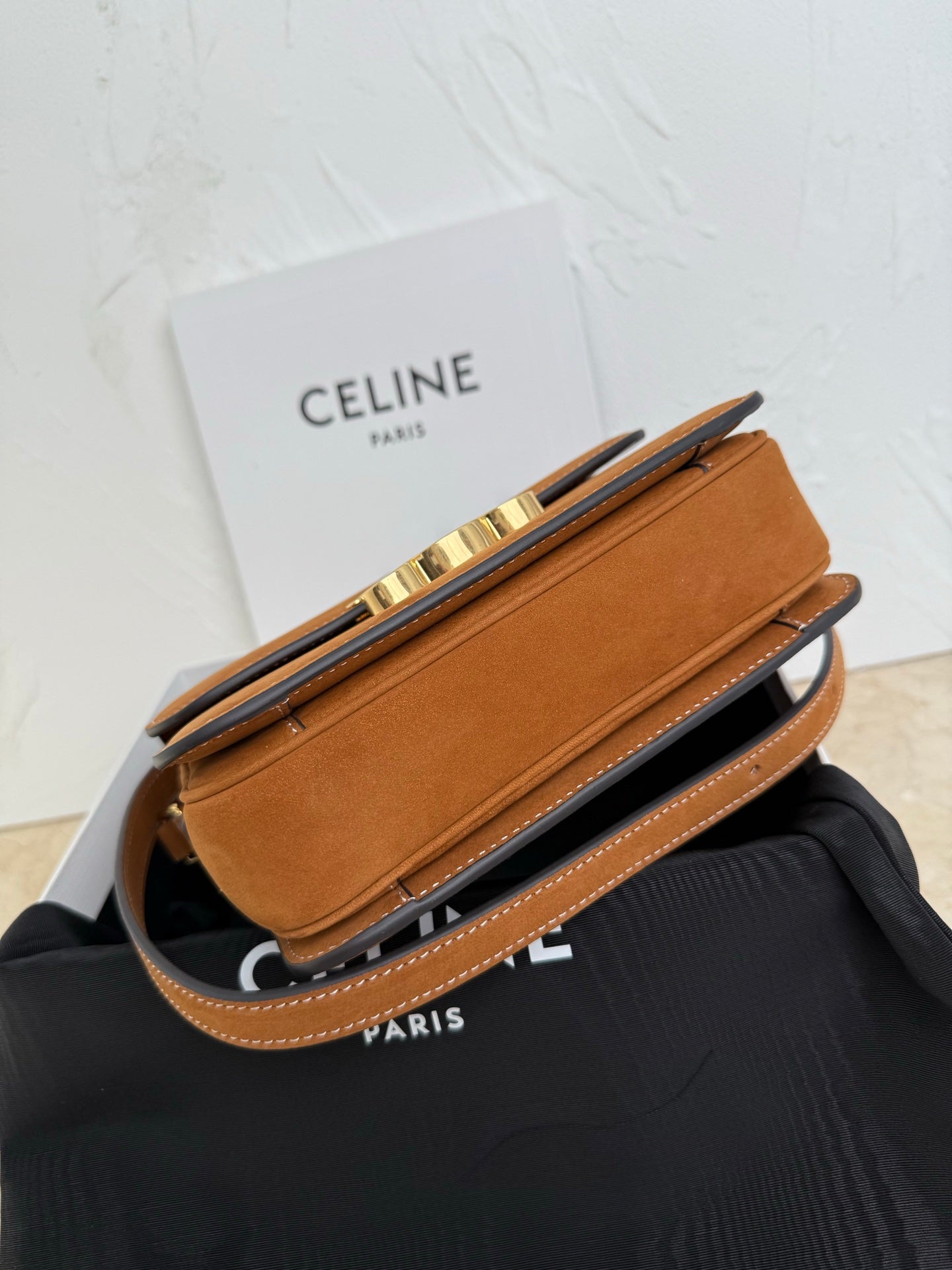 Tan suede bag with flap closure and gold-tone hardware; shown at angle with strap.