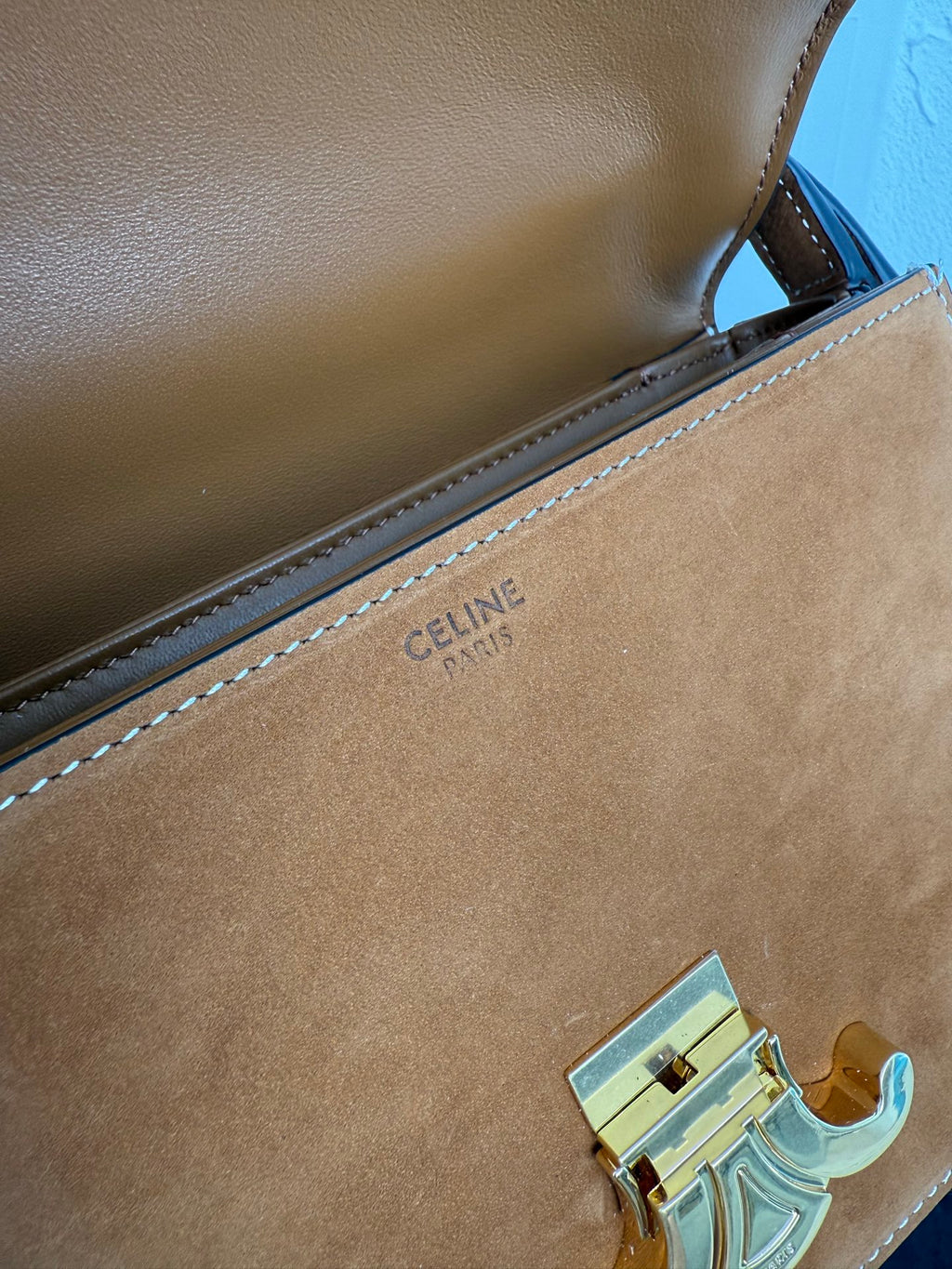 Tan leather bag with inner brand stamp on the edge seam and gold-tone emblem hardware.