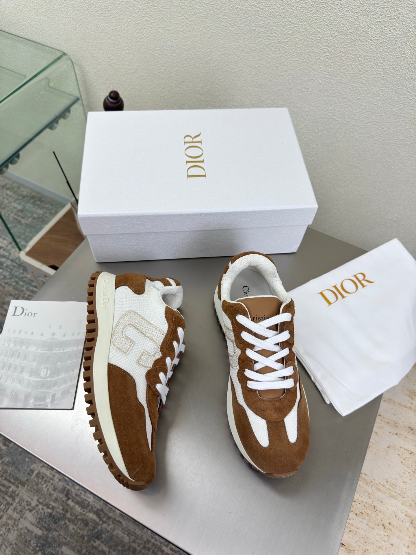 Brown and white sneakers with white laces and thick sole, pair next to dust bag
