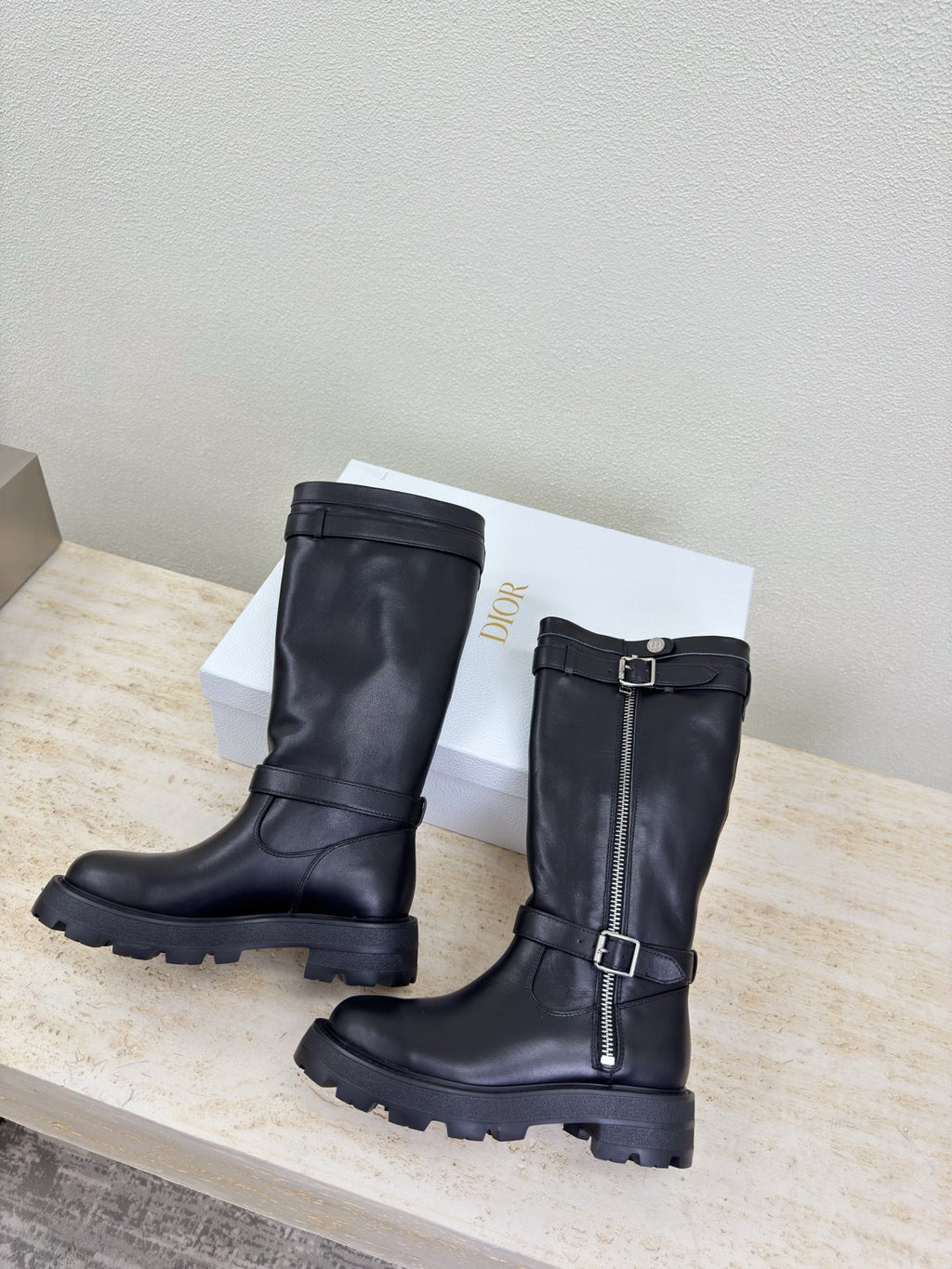 Two black knee-high boots with buckle strap and side zipper, angled view