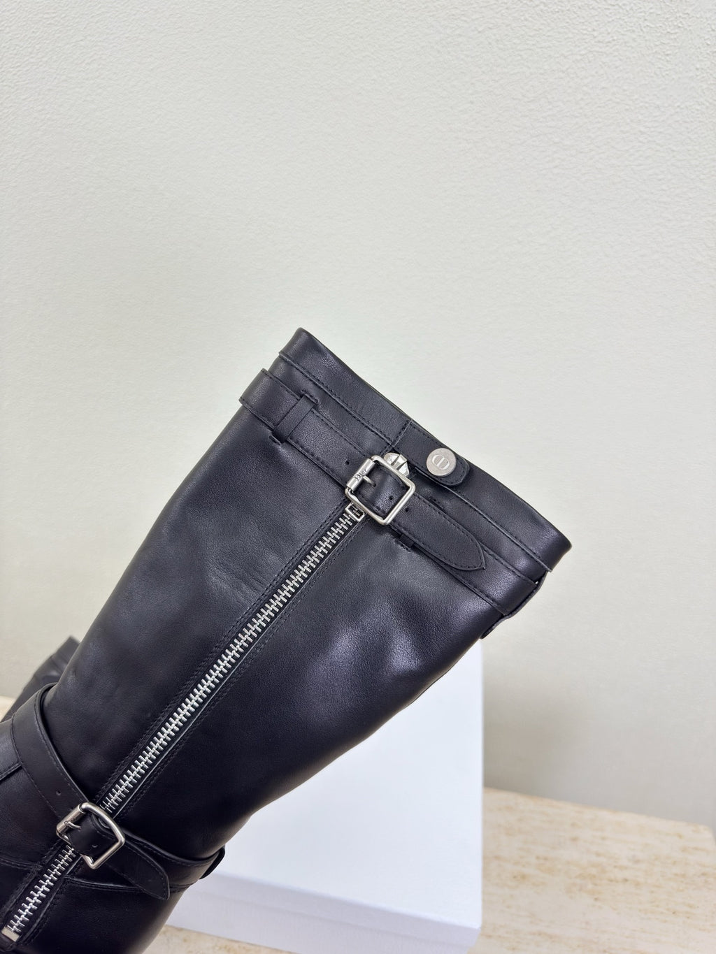 Black knee-high boot with side zipper and double buckle straps, close-up