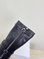 Black knee-high boot with side zipper and double buckle straps, close-up