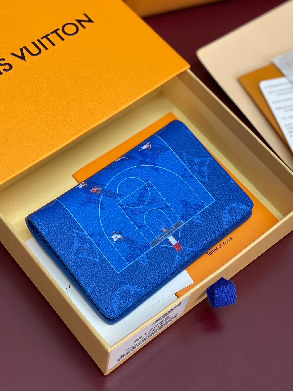 Blue small bag with printed motif and smooth flap, shown on its box