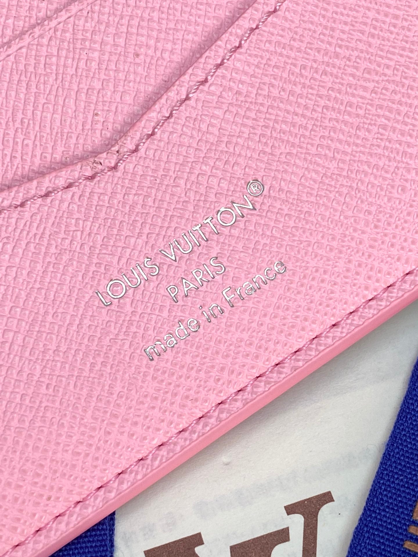 Close-up of pink small bag corner with Louis Vuitton Paris badge and stitching