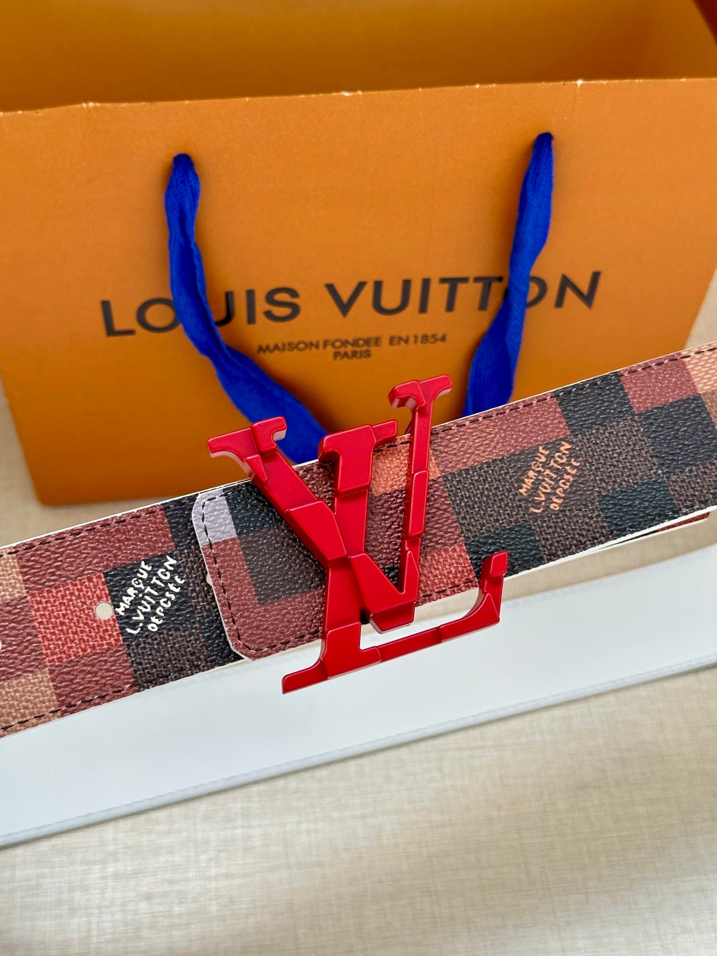 Louis Vuitton belt buckle: red V emblem over checkered strap, close-up