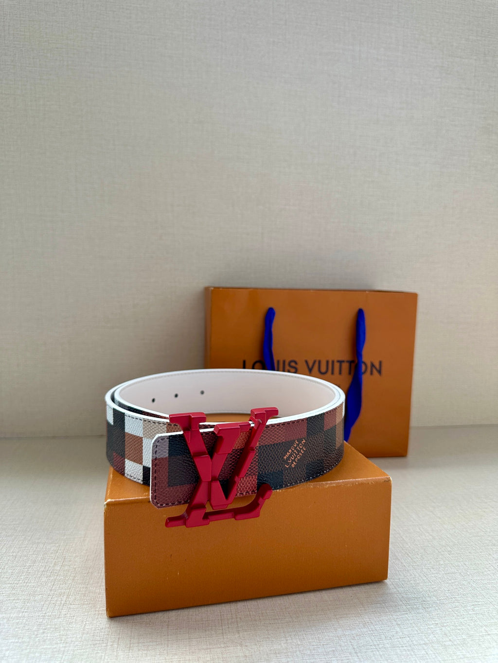 Louis Vuitton checkered belt with red V buckle on white strap, angled view