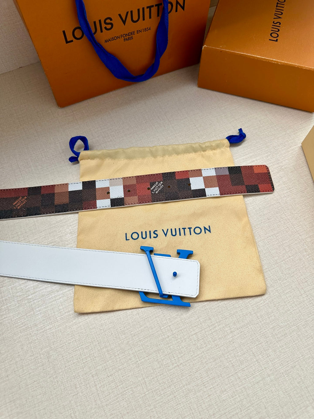 Louis Vuitton belt with checkered strap and blue LV buckle, plus beige dust bag