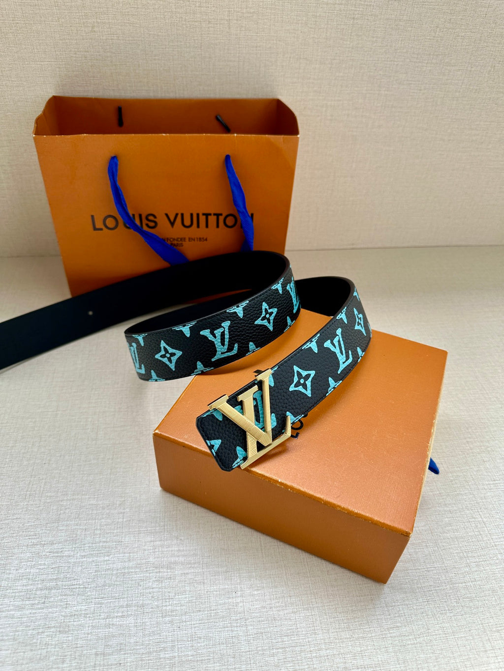 Louis Vuitton belt laid out with dark navy and turquoise monogram strap, gold buckle