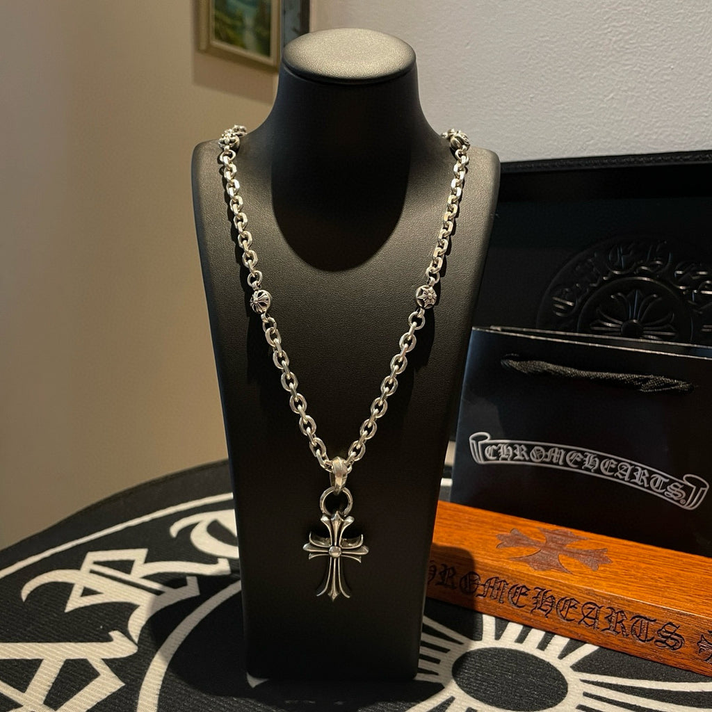 Silver cross pendant necklace with curb-style chain on a display bust