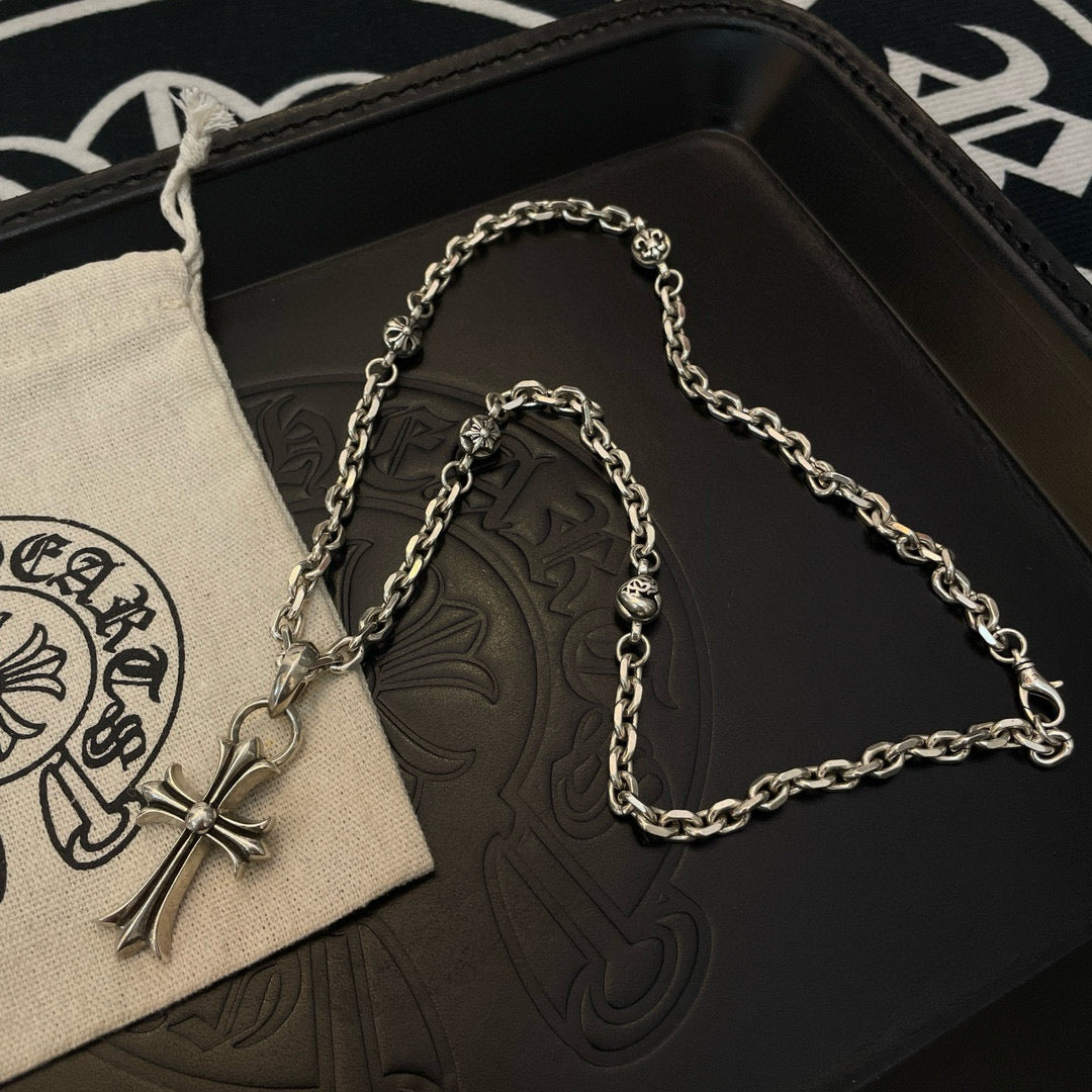 Silver cross pendant necklace with curb chain on black tray and pouch