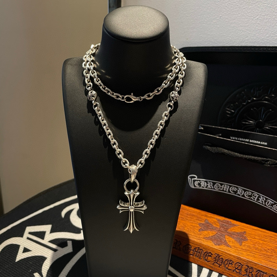 Silver cross pendant necklace with layered curb chain on display bust