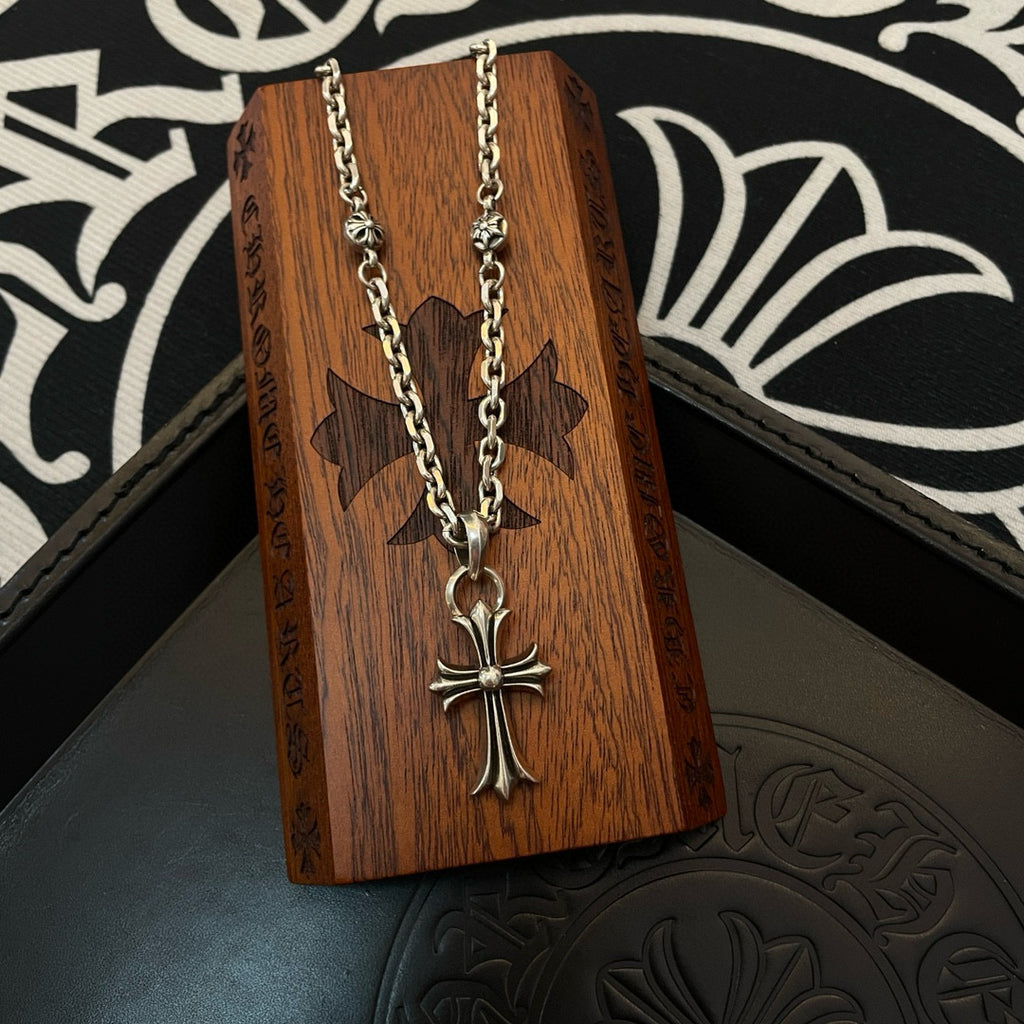 Silver cross pendant necklace with curb chain on a wooden panel