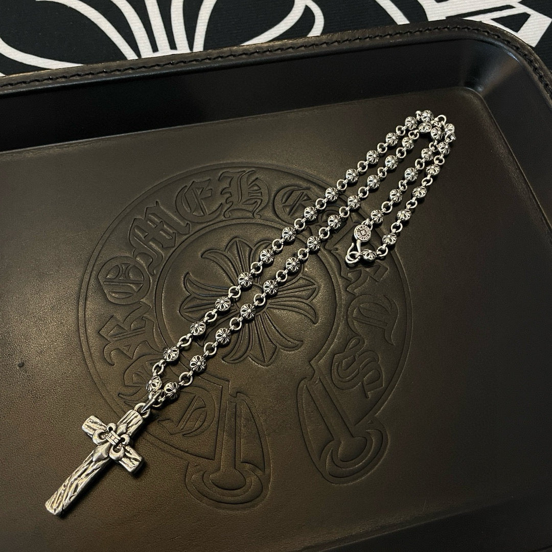 Silver-tone cross pendant necklace draped on embossed leather tray