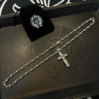 Silver-tone cross pendant necklace with velvet pouch on embossed leather tray