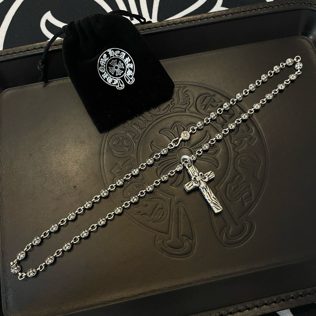 Silver-tone cross pendant necklace with velvet pouch on embossed leather tray