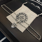 Heart pendant necklace with silver-tone chain on black case beside cloth pouch
