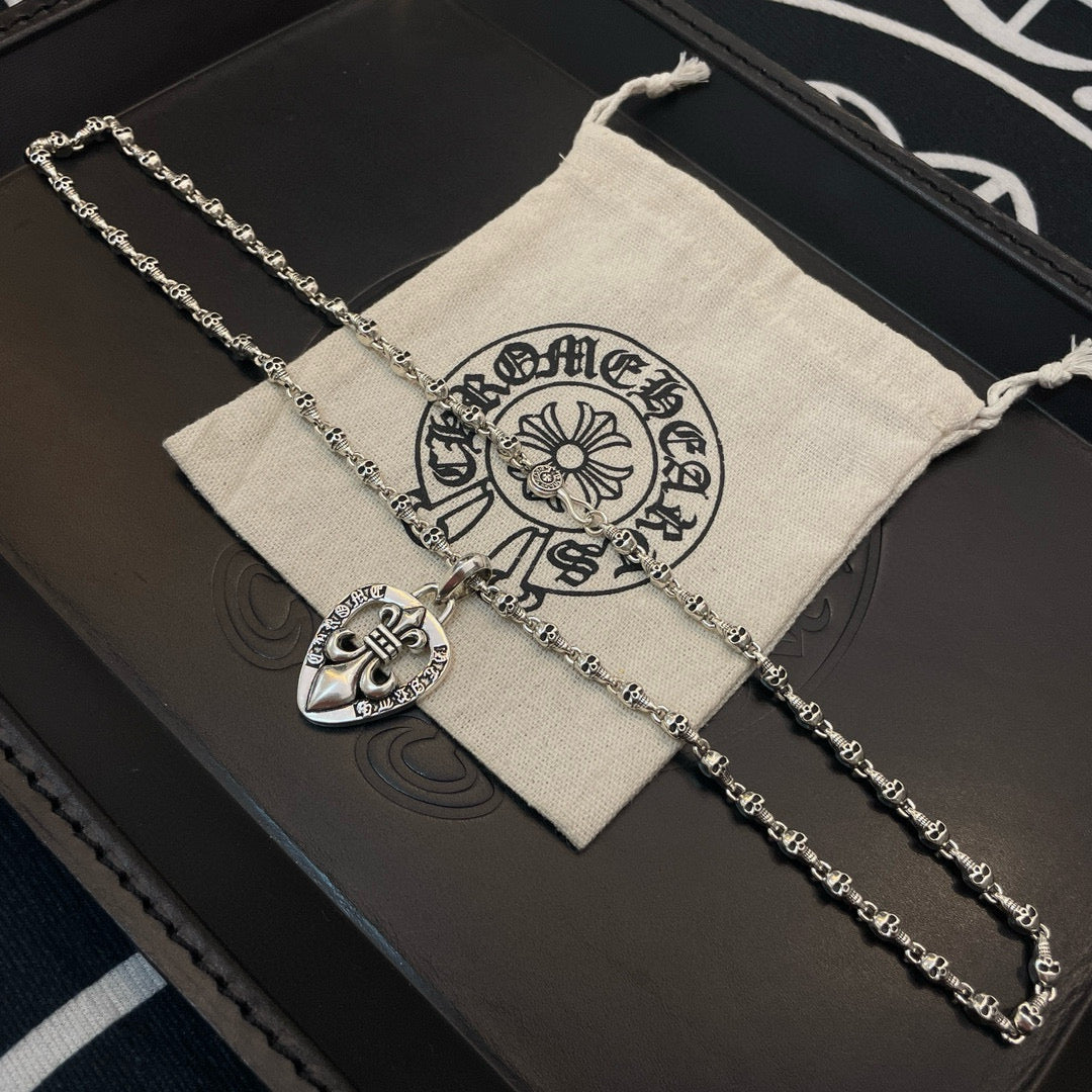 Heart pendant necklace with silver-tone chain on black case beside cloth pouch