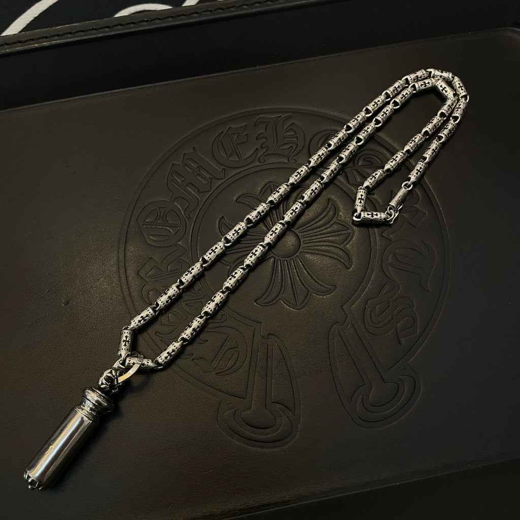Silver-toned charm necklace with cylinder pendant, shown on a dark leather box