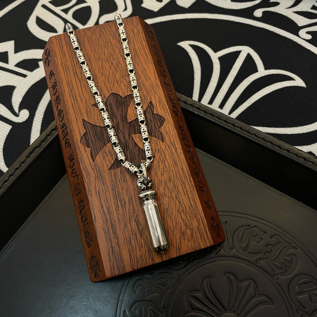Silver-toned charm necklace with cylinder pendant hanging over a wood display piece