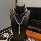 Silver-toned charm necklace with central drop pendant on a black mannequin stand