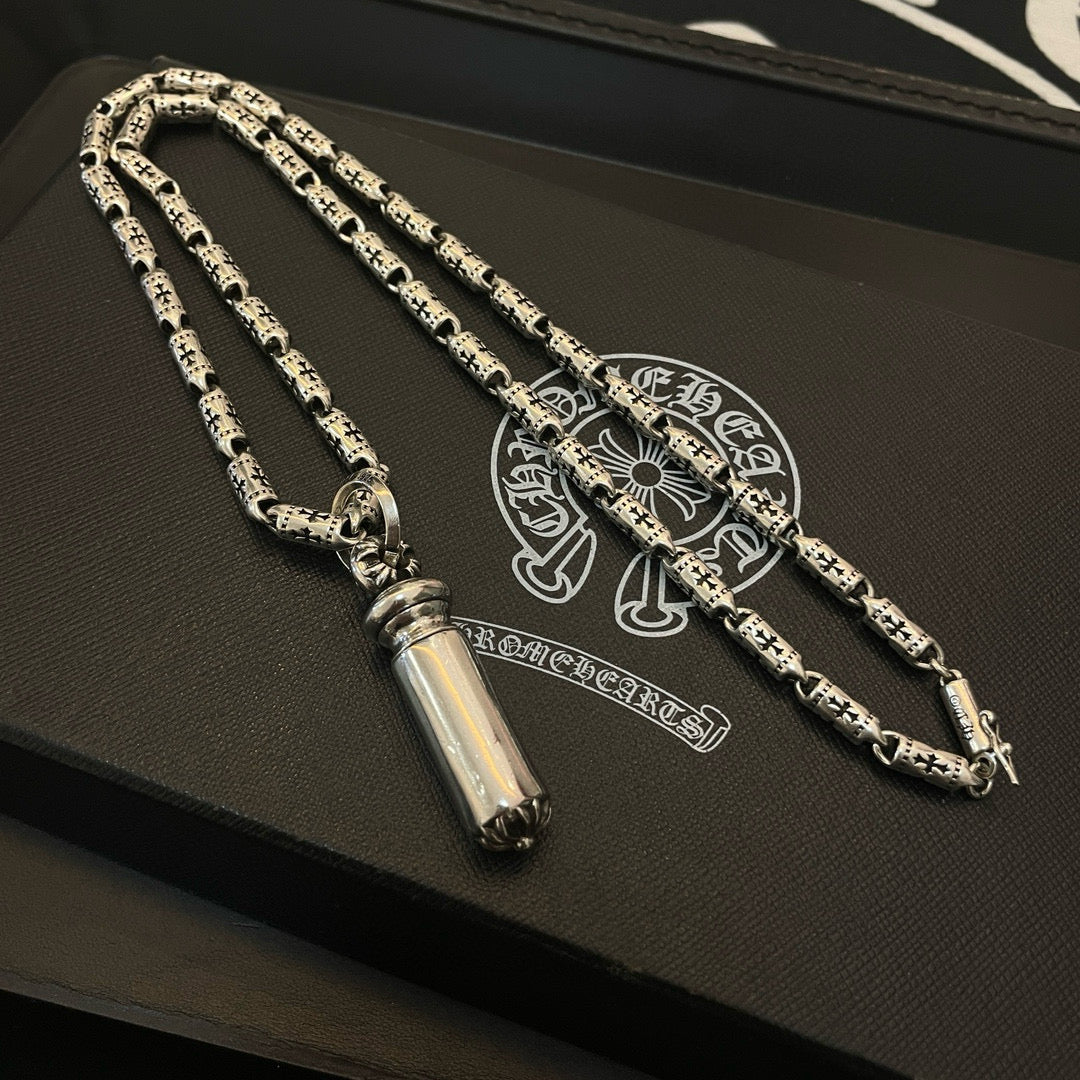 Silver-toned charm necklace set on a dark jewelry box with printed emblem