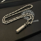 Silver-toned charm necklace with cylinder pendant, laid on a dark leather box