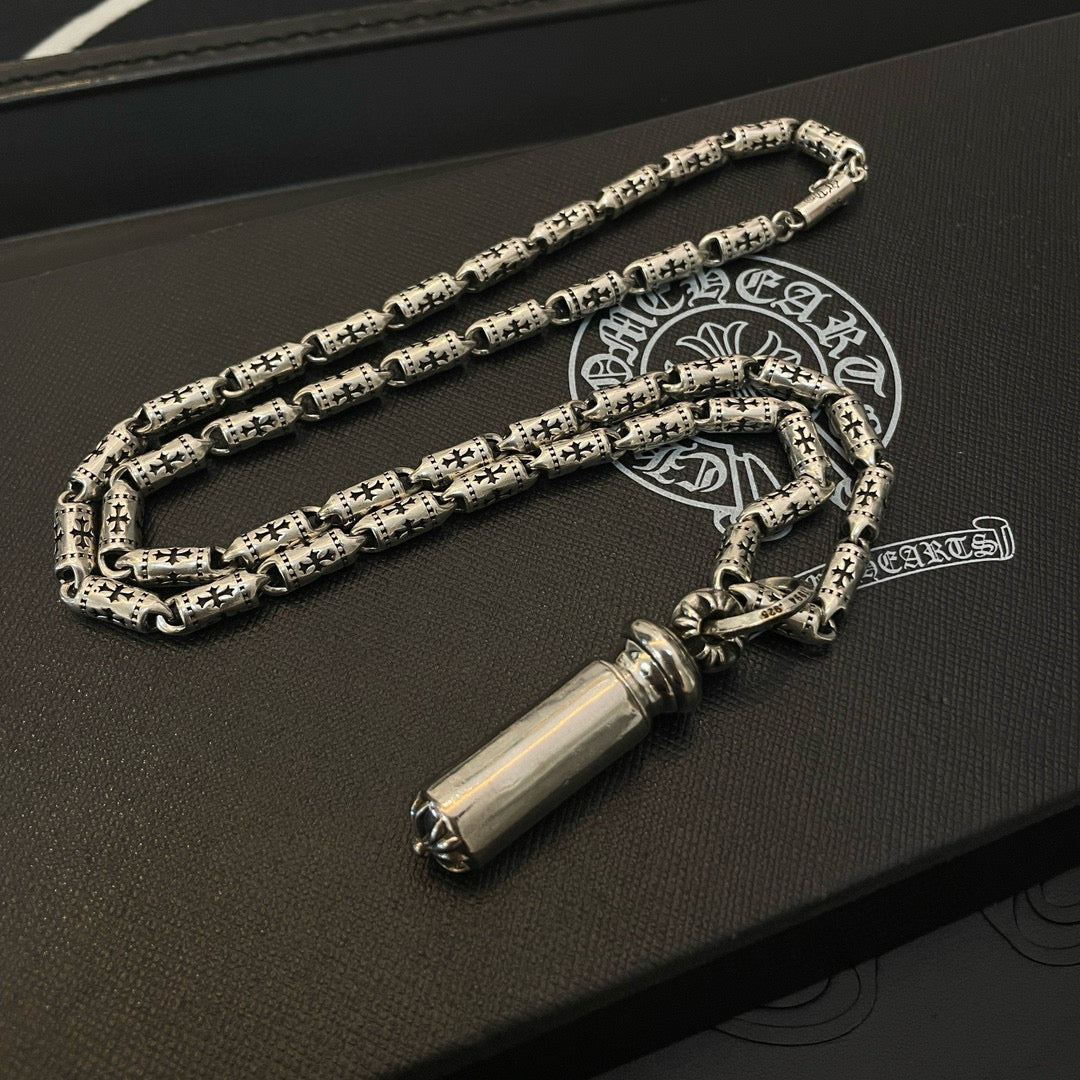 Silver-toned charm necklace with cylinder pendant, laid on a dark leather box