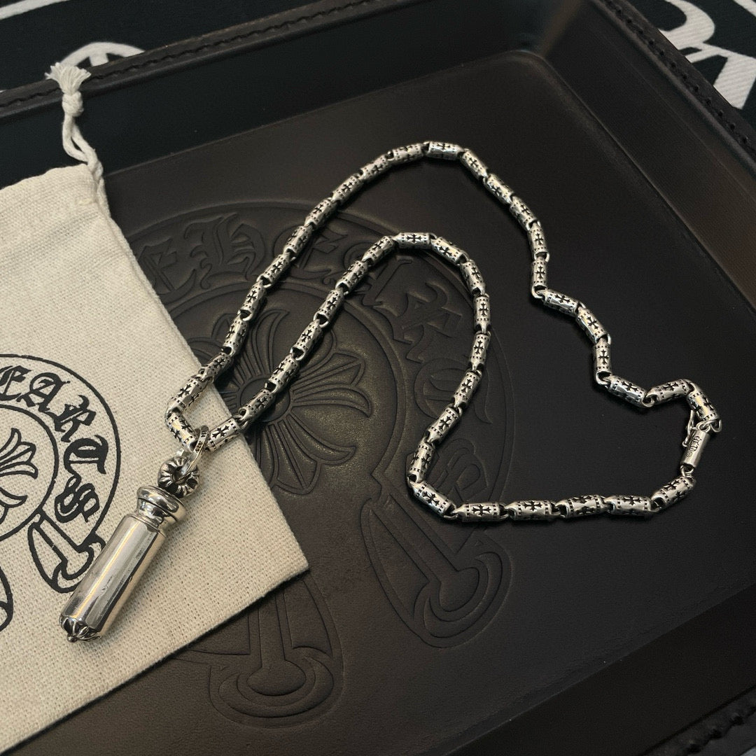 Silver-toned charm necklace with cylinder pendant, coiled on a black box