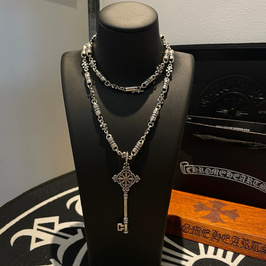 Key pendant necklace with silver chain and fleur-shaped cross charm on bust display