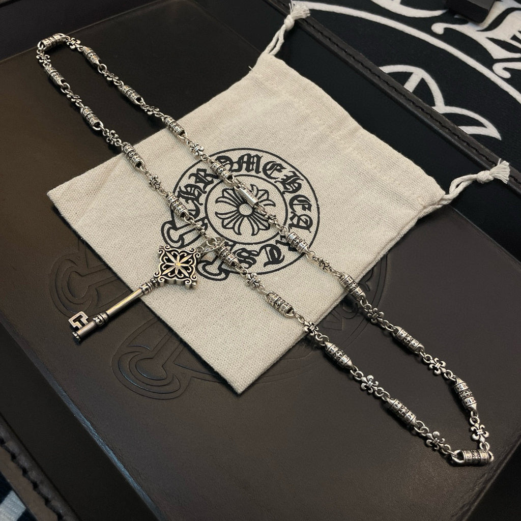 Key pendant necklace resting on beige pouch with printed emblem and white drawstring