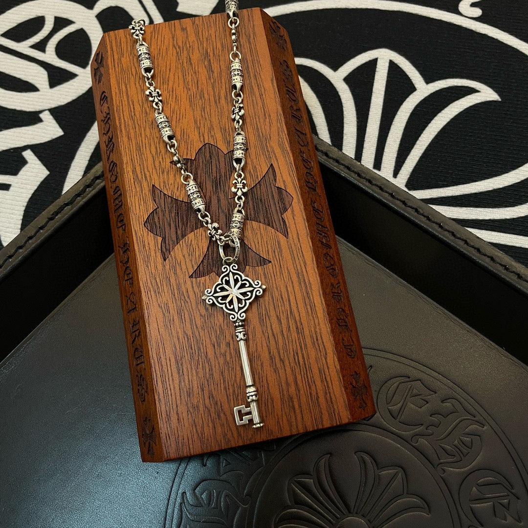 Key pendant necklace on small wooden stand, silver chain with fleur cross charm