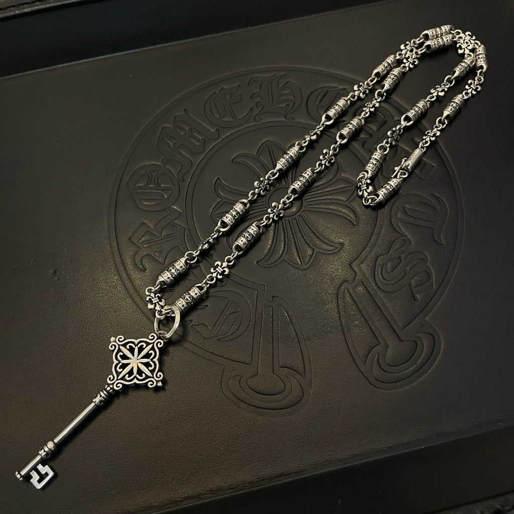 Silver-tone key pendant necklace with chain, fleur charm, and engraved bead details