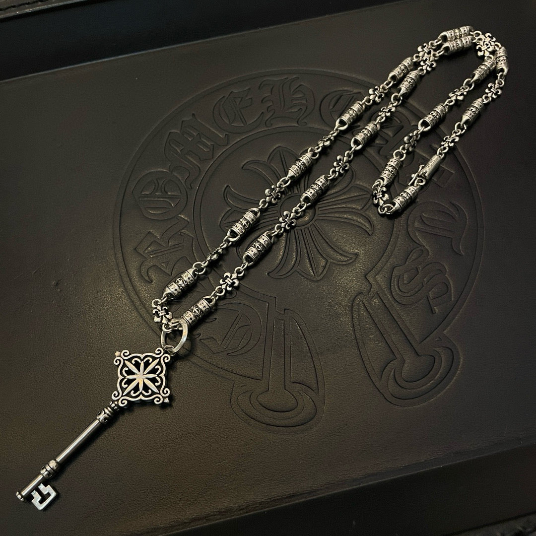 Silver-tone key pendant necklace with chain, fleur charm, and engraved bead details
