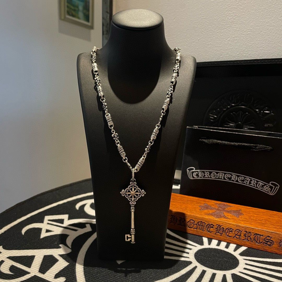 Key pendant necklace with chain and cross-style centerpiece, displayed on black bust form