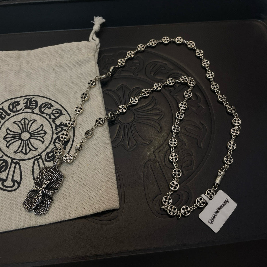 Silver beaded chain necklace with pendants on dark case beside beige pouch