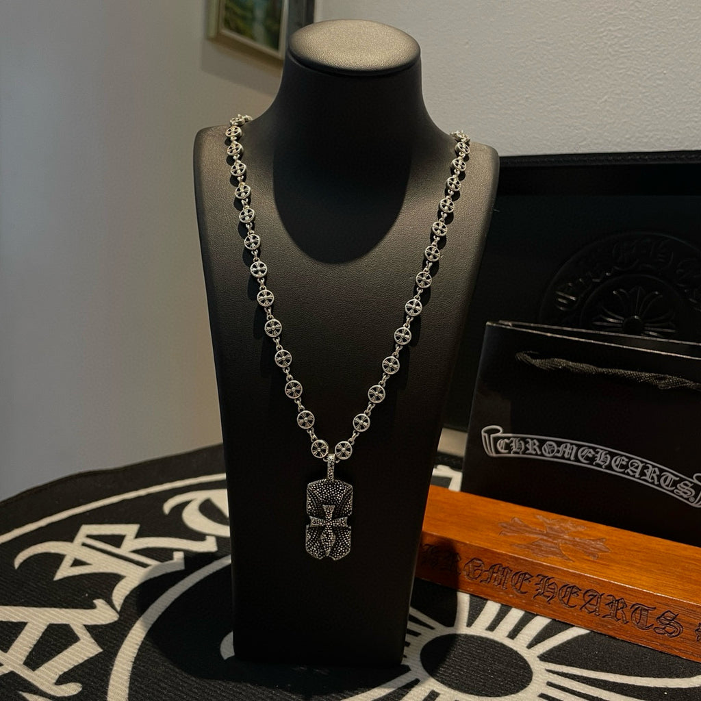 Silver beaded chain necklace with cross-like pendant on black display bust