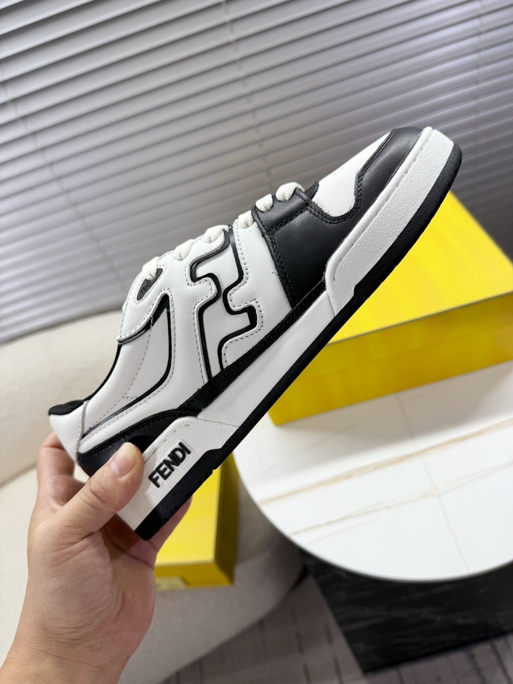 White and black lace-up low-top sneakers held in hand, side logo detail
