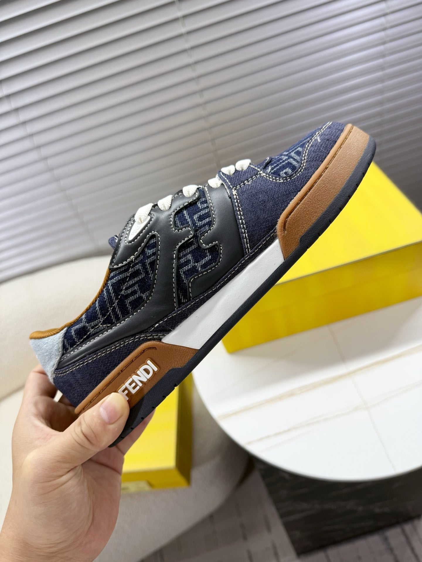 Navy Fendi sneakers, hand-held side view with FF logo and brown rubber sole.