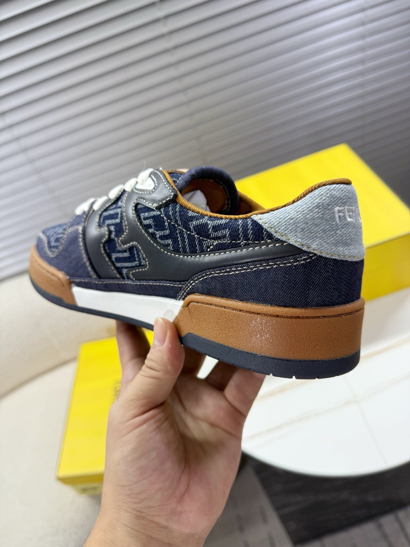 Navy Fendi sneakers, hand-held heel view with tan sole edge and blue upper details.