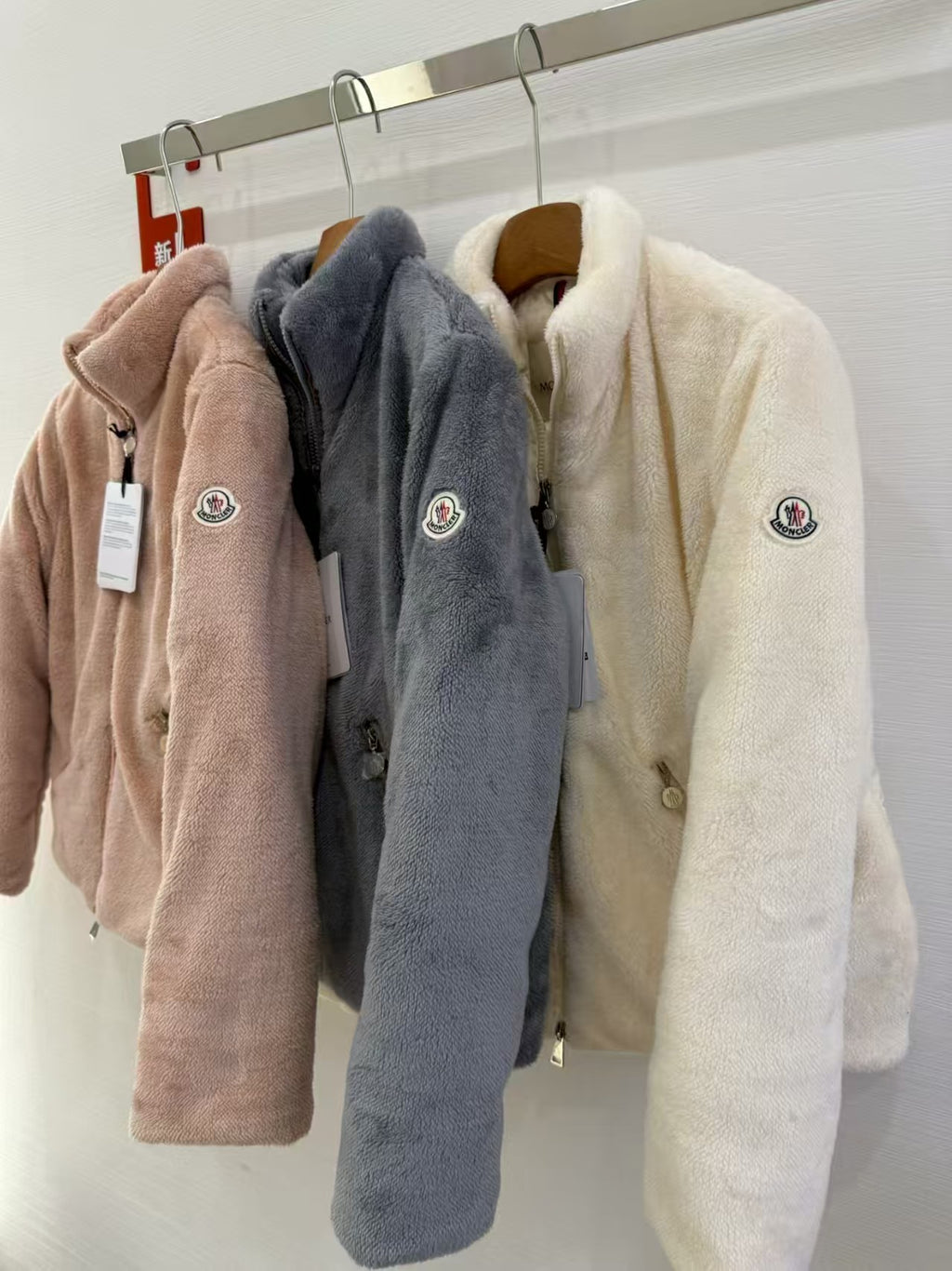 Long-sleeve zip fleece jackets with hood in tan, charcoal, and cream on hangers