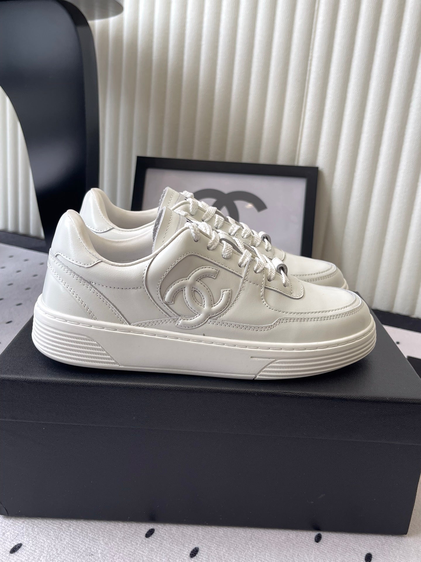 White leather lace-up sneaker on black box, side profile with Chanel emblem